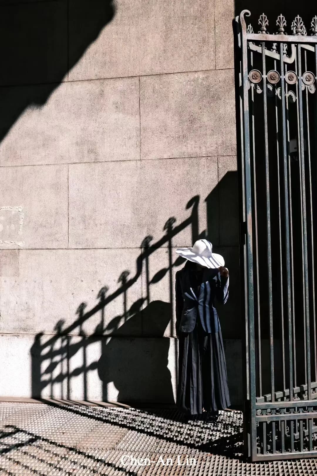 A figure beside an iron gate and angular shadows.